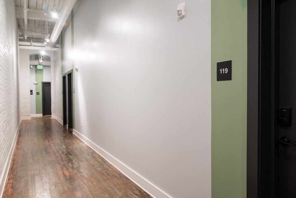 a hallway with white walls and wood floors and a green door