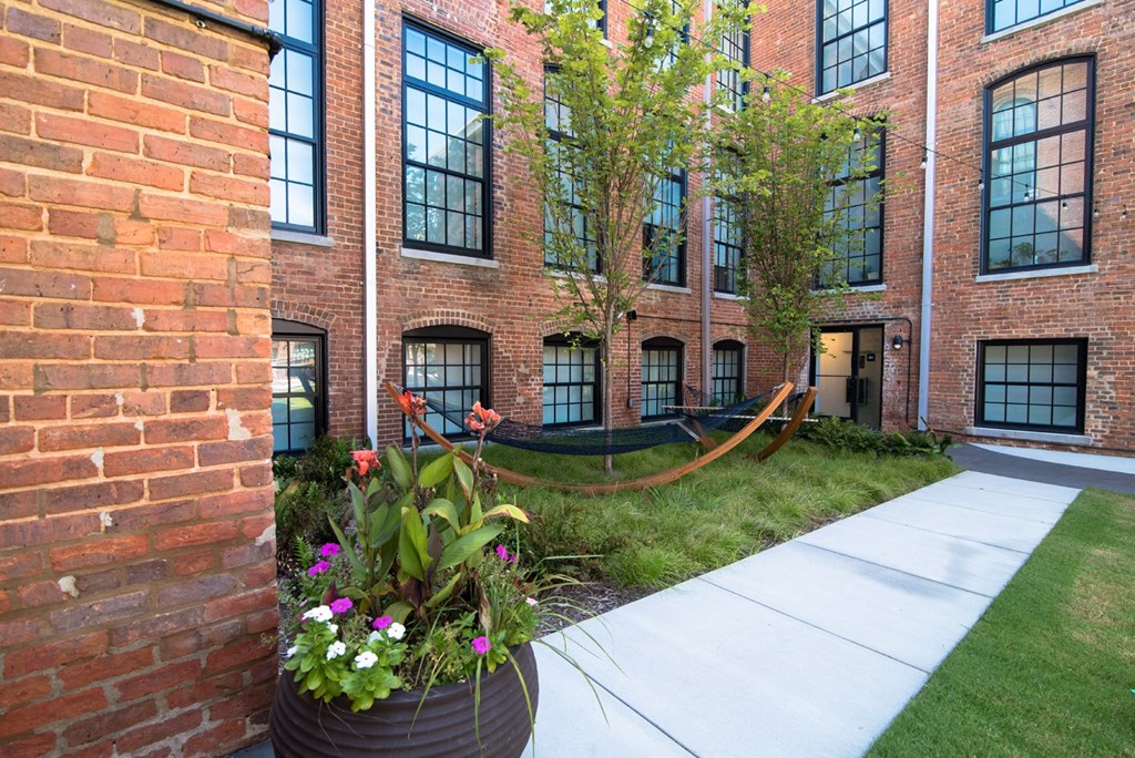 the yard of a brick building with a hammock and flowers in front of it