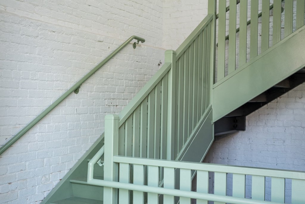 a stairwell with white stairs and green railing and a white brick wall
