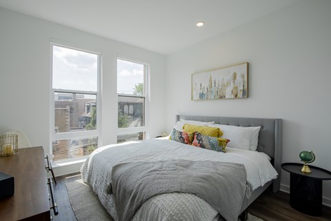 Modern bedroom at The Rail Bound Brook with three large windows, city views, and a cozy bed—offering comfort and elegance in NJ apartment living.