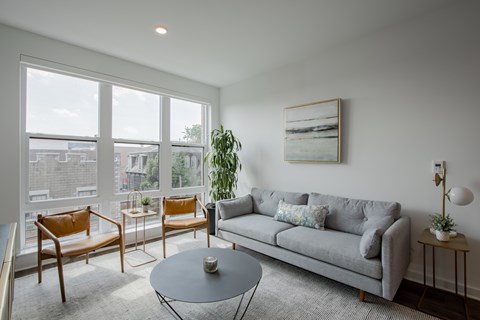 Contemporary living space at The Rail with modern furnishings, large rug, and natural finishes—ideal for urban lifestyle near NJ Transit.