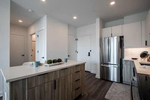 Entryway and modern kitchen with woodgrain cabinets, quartz countertops, and an island at The Rail Bound Brook—combining style with functionality.