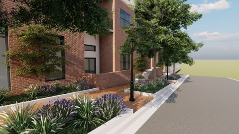 A street view of a building with a brick facade and a sidewalk lined with plants and a lamp post.