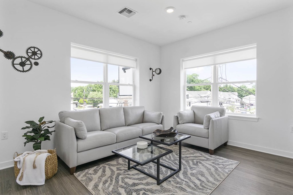 A living room with a white couch, a glass coffee table, and a wall clock at 10 N. Main Apartments, Wharton, NJ, 07885