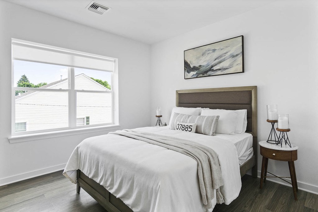 A bedroom with a large bed and a window overlooking a house at 10 N. Main Apartments, New Jersey