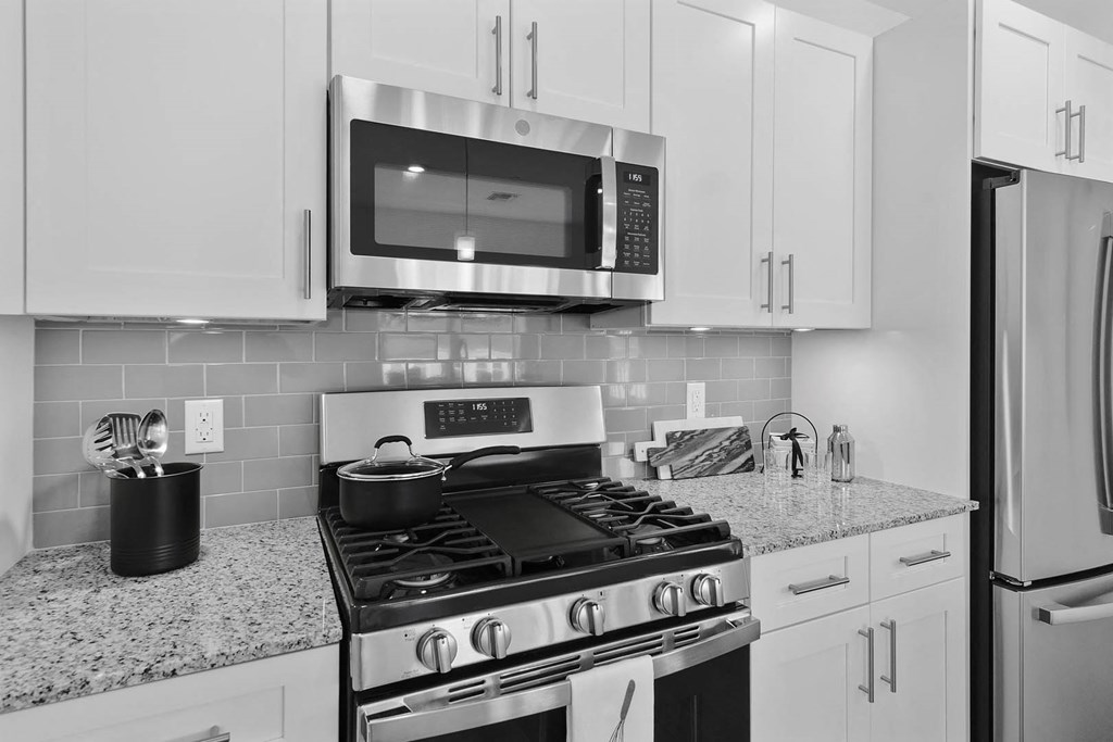 A black and white image of a kitchen with a stove, microwave, and refrigerator at 10 N. Main Apartments, Wharton