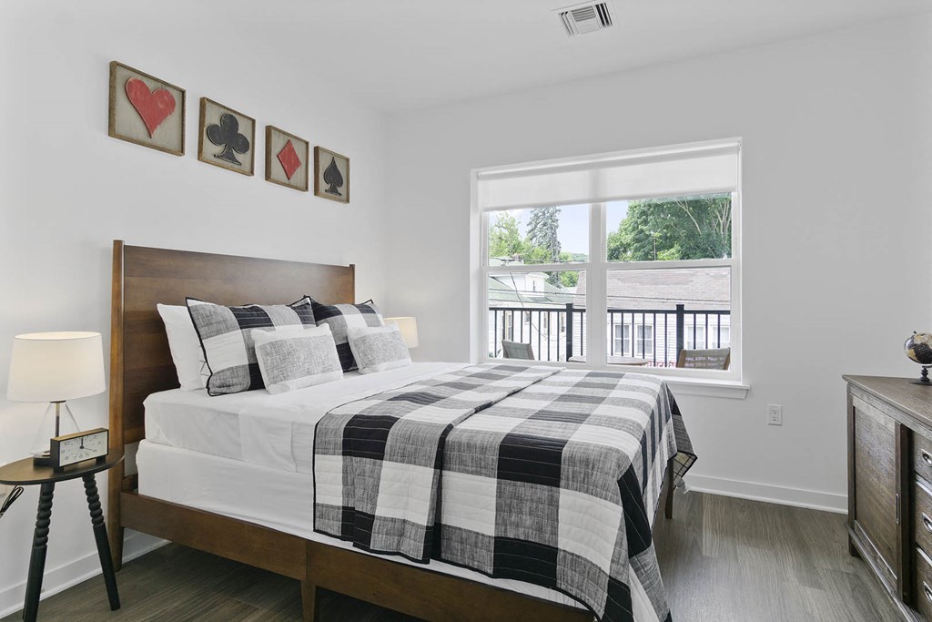 A bedroom with a bed, a nightstand, and a window overlooking a deck at 10 N. Main Apartments, Wharton, NJ
