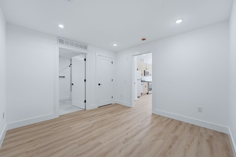 A white room with wood flooring and a doorway leading to another room.