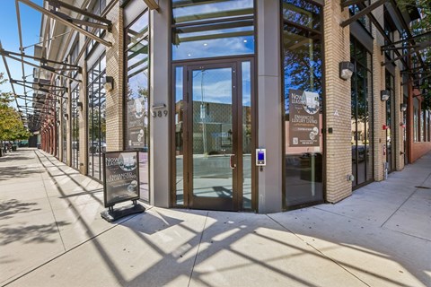 The image shows a modern building entrance with a glass door and a sign that reads "Now Open".