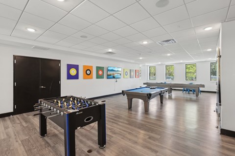 A foosball table is in the middle of a room with a pool table and pictures on the wall.