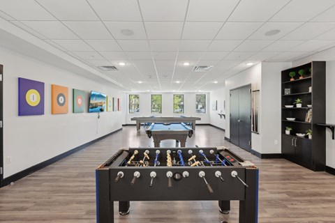 A foosball table is in the middle of a room with a pool table and pictures on the wall.