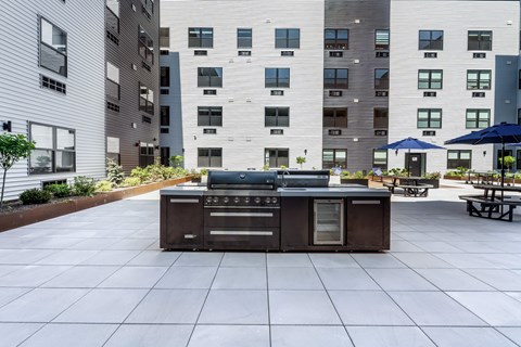 A BBQ grill is in the middle of a courtyard surrounded by buildings.