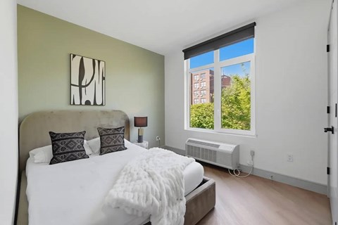 A bedroom with a large bed and a window overlooking a green area.