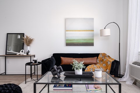 A living room with a black couch and a painting on the wall.