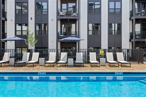 A pool with chairs and umbrellas in front of a building.
