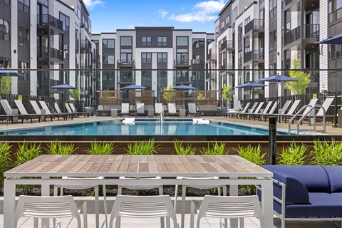 A pool surrounded by chairs and tables in front of apartment buildings.