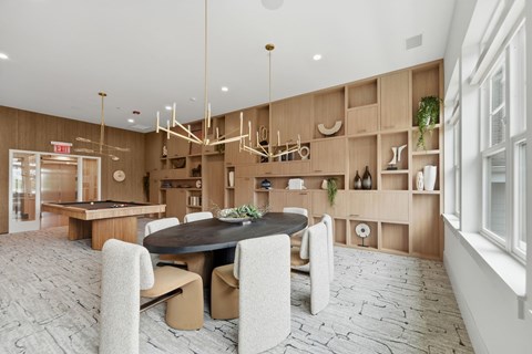 A Clubroom with a round table surrounded by chairs and a shelf with various items on it.
