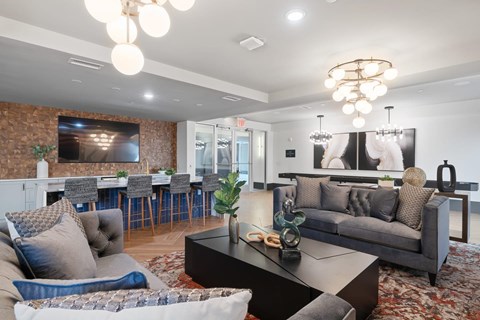 A modern living room with a grey couch, a coffee table, and a dining area in the background.