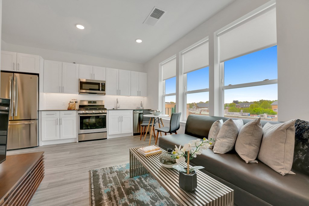 a living room with a couch and a coffee table and a kitchen with a refrigerator