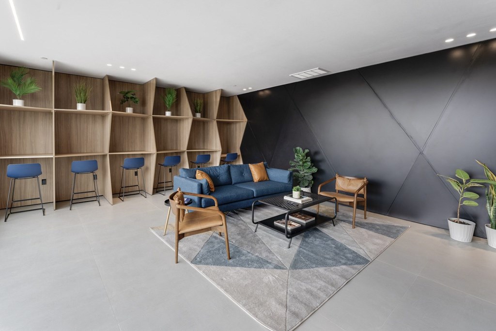 A modern living room with a blue sofa, wooden chairs, and a grey rug.