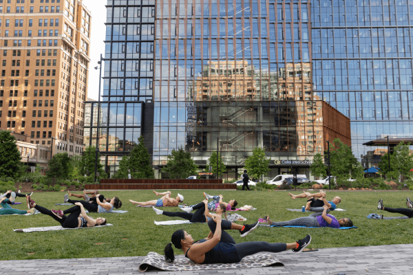 A group of people doing yoga in a park with a glass building in the background.