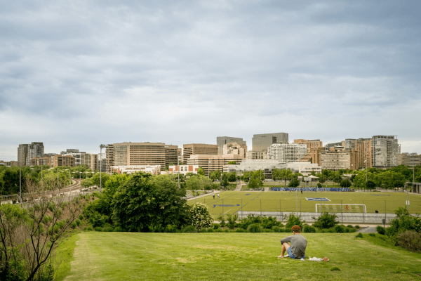 A man sits on a grassy hill overlooking a city skyline.
