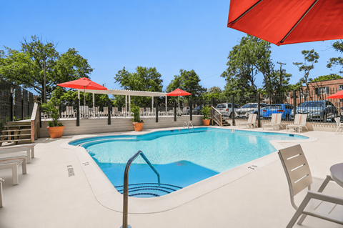 A large outdoor swimming pool with red umbrellas and lounge chairs.