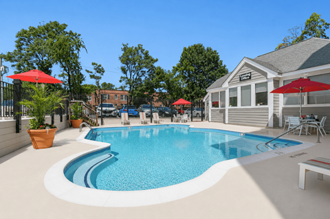 A pool with a red umbrella and a white bench.