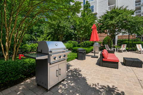 A BBQ grill is in the middle of a patio surrounded by furniture.