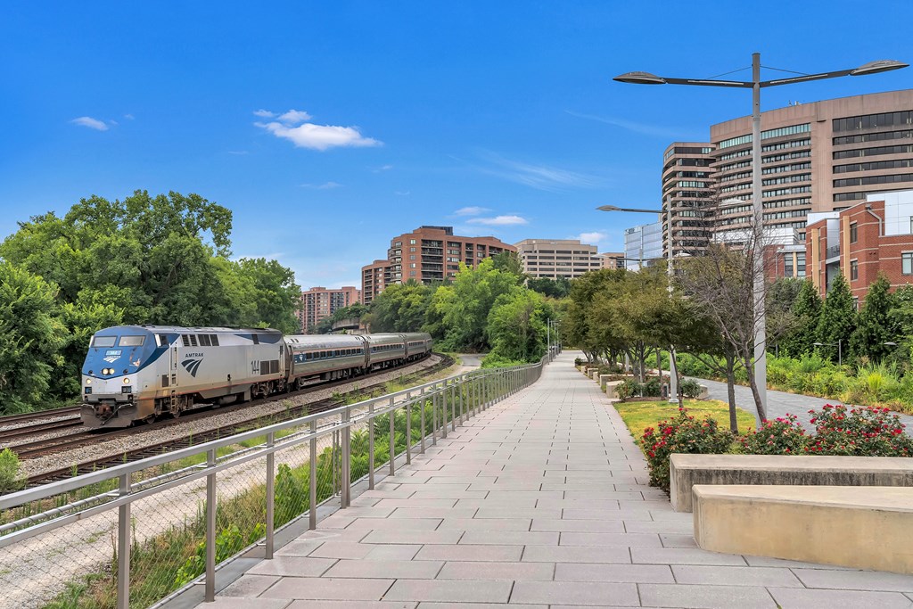 a train on the tracks near a sidewalk with trees and buildings