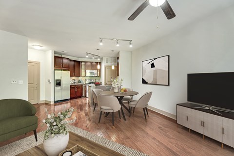 A modern living room with a green armchair, a dining table set for four, and a television on the wall.