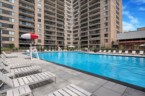 A swimming pool with sun loungers and a red umbrella in front of apartment buildings.