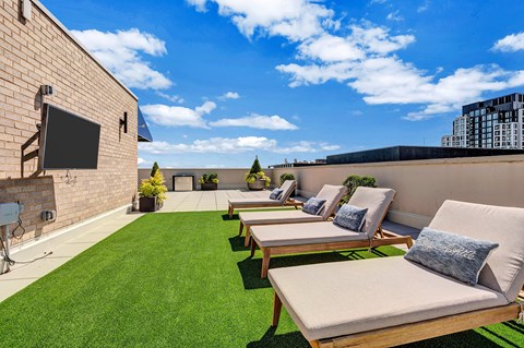 A sunny rooftop patio with a row of lounge chairs and a flat screen TV.