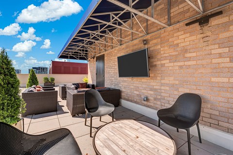A patio with a table, chairs and a television on a brick wall.