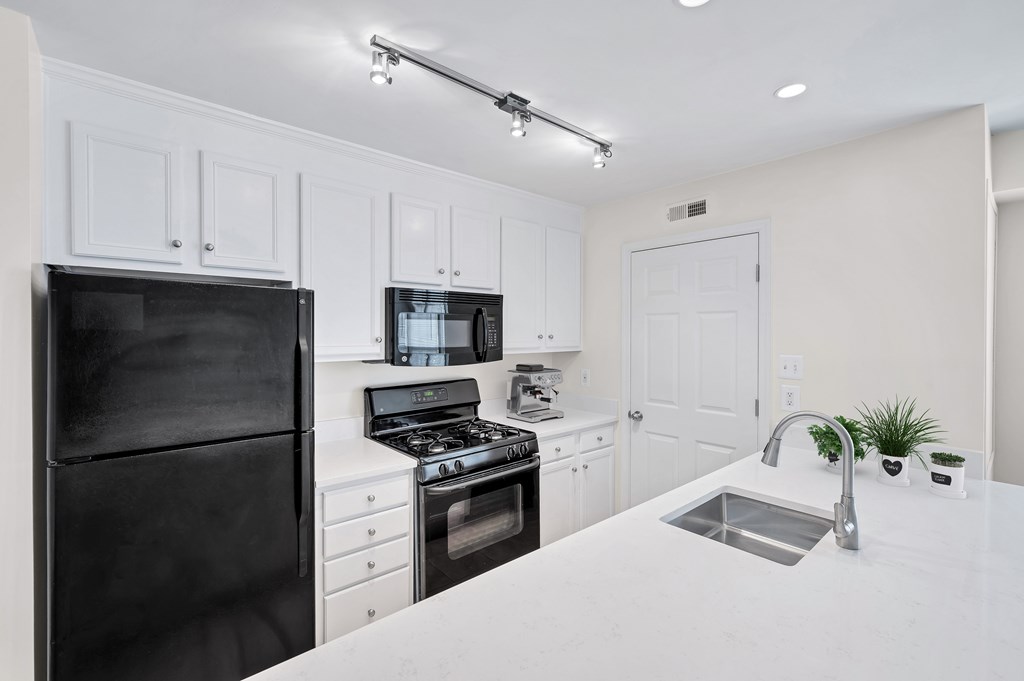 A black refrigerator is on the left in a white kitchen.