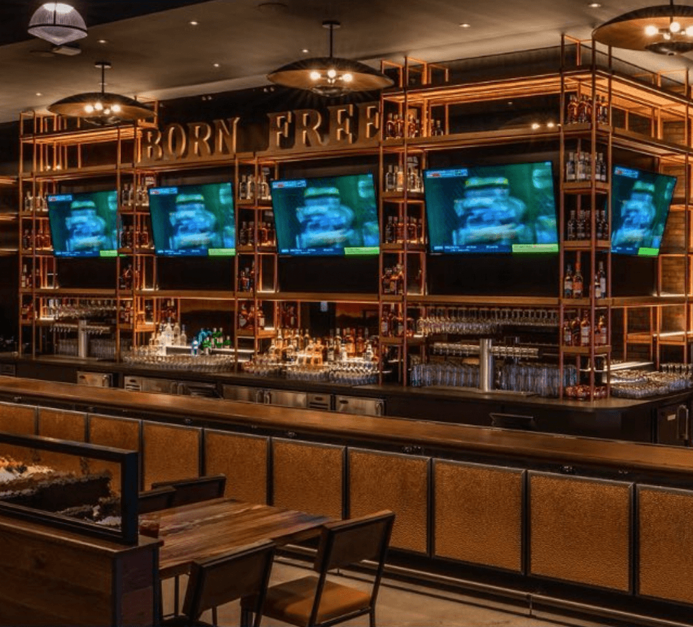 a bar with tvs on the wall and wooden tables and chairs