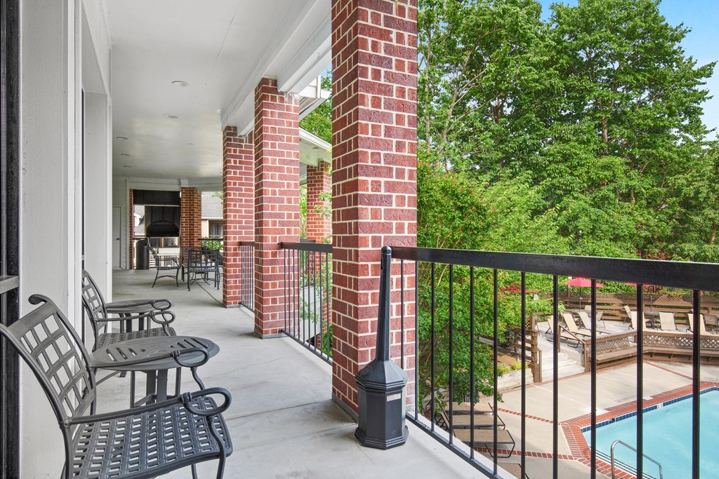 a balcony with two chairs and a table and a pool in the background