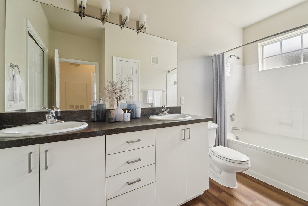 A white bathroom with a double sink and a toilet.