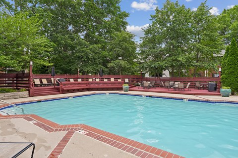 A large outdoor swimming pool surrounded by trees and a red fence.