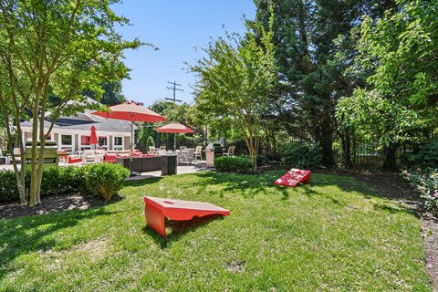 A red bench sits in a grassy area with trees and a building in the background.