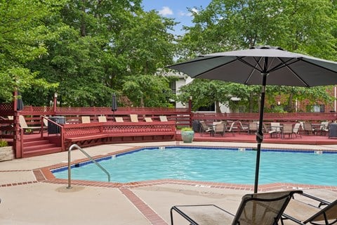A pool with a red bench and a black umbrella.