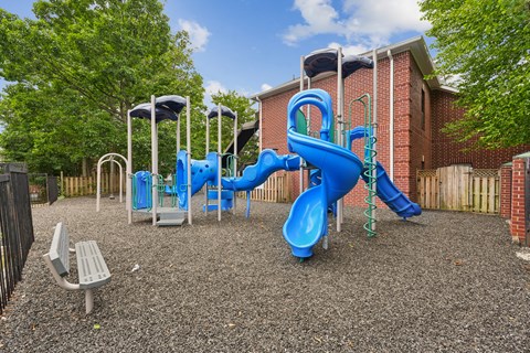 A playground with a blue slide and a grey bench.
