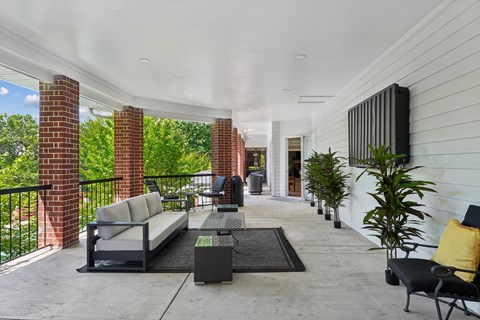 A patio with a black couch and a black chair with a yellow pillow.