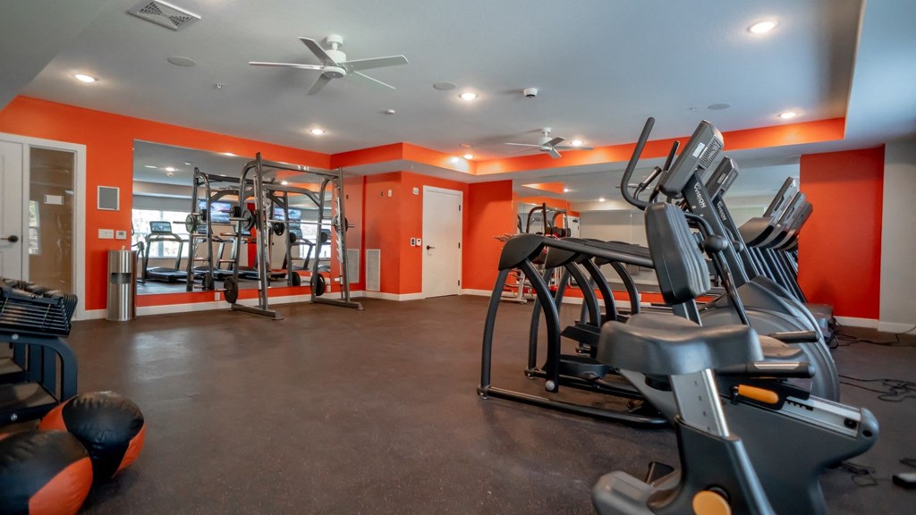A gym with orange walls and a variety of exercise equipment.