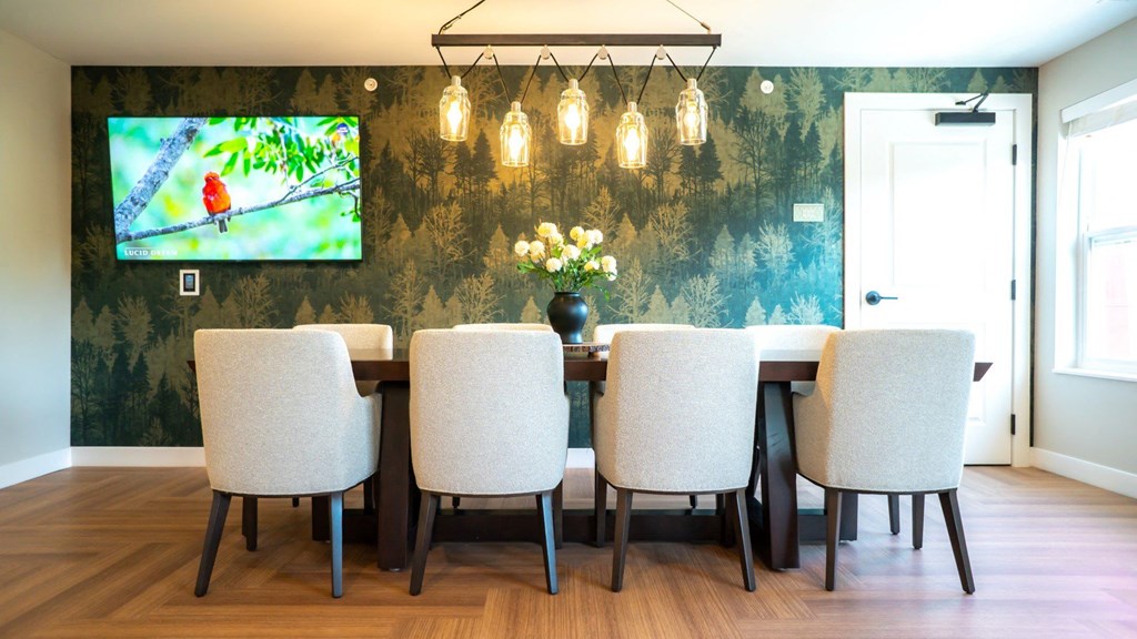 A dining room with a television mounted on the wall and a vase of flowers on the table.
