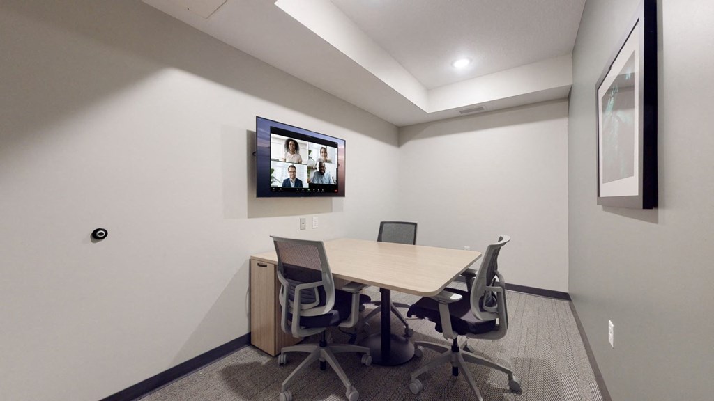 A conference room with a table, chairs and a screen on the wall.