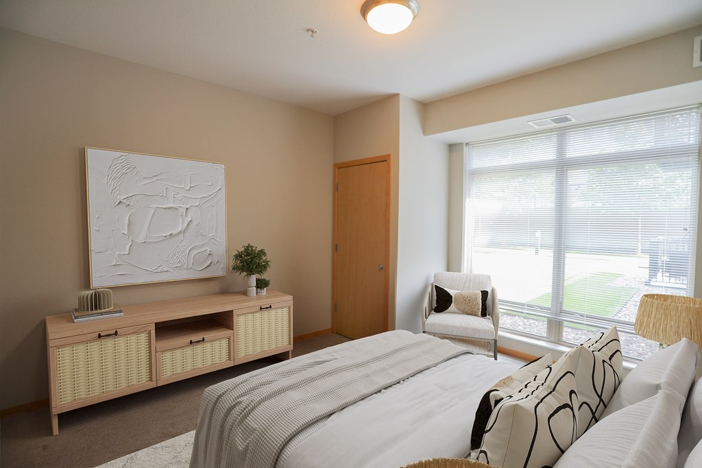 a bedroom with a large window and a bed with a white comforter