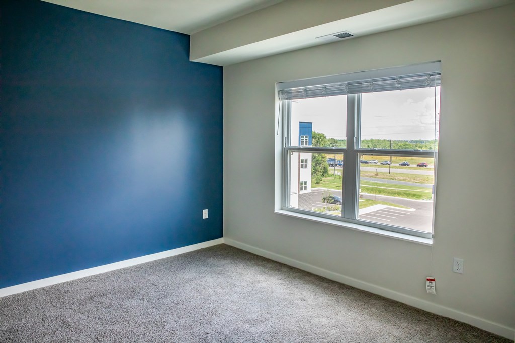 a bedroom with a large window and carpeted flooring