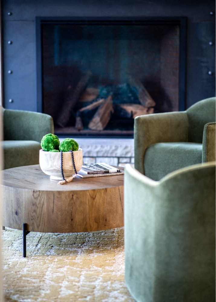 a coffee table with two green chairs in front of a fireplace