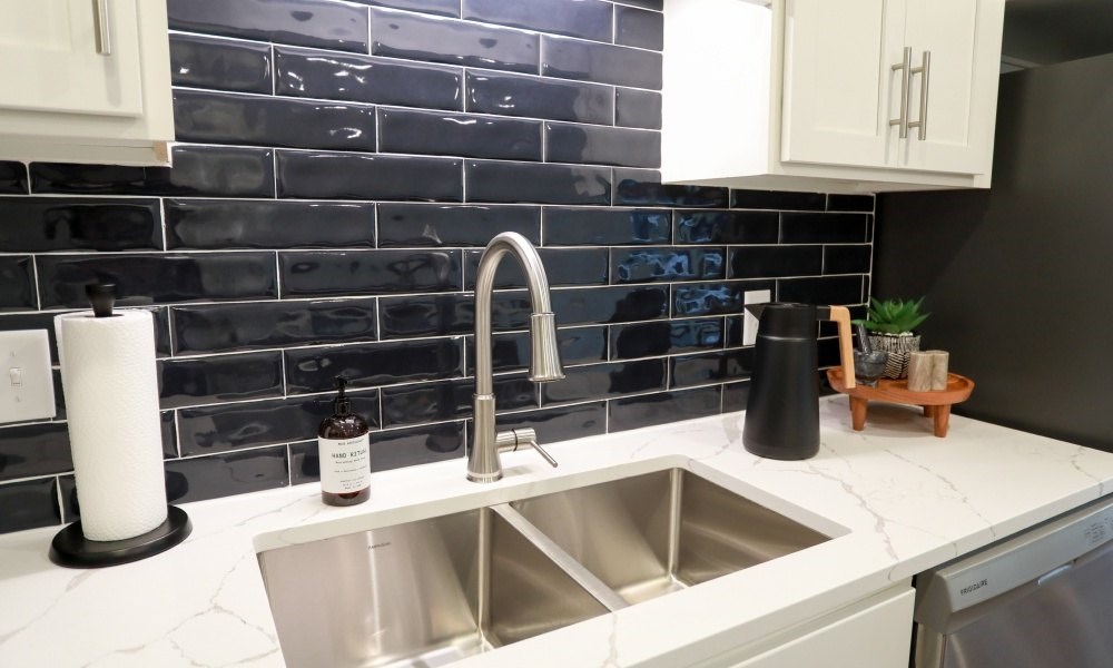 A kitchen with a sink and a black tiled backsplash.